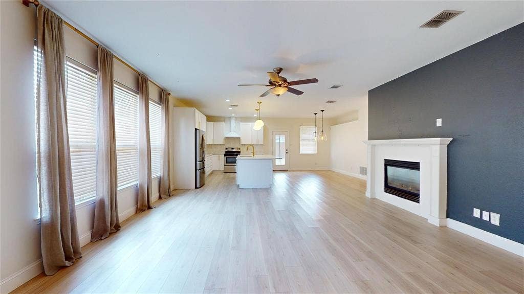 10514 Greenbriar Lane, Rowlett, TX 75089 Open-concept living space featuring wood-finish flooring, a wall-mounted electric fireplace with a white mantel, kitchen island with quartz-style countertop, white cabinetry, and large windows with natural light