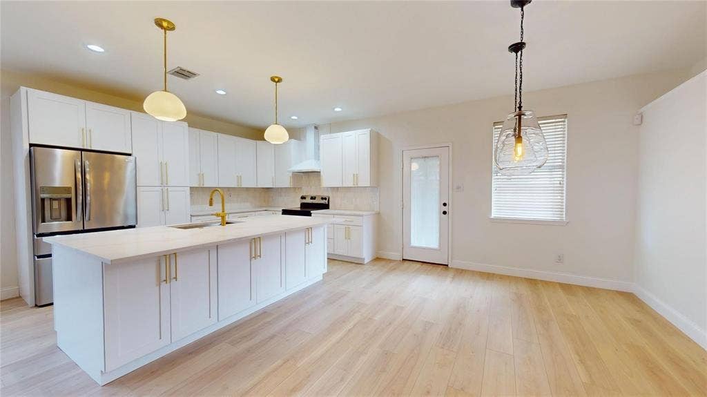 10514 Greenbriar Lane, Rowlett, TX 75089 Kitchen featuring white shaker-style cabinetry, quartz countertops, an expansive center island with gold-finish hardware, stainless steel appliances, and wood-finish flooring