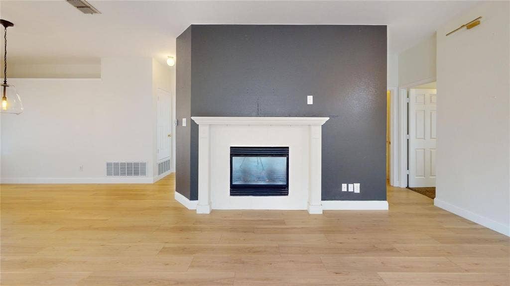 10514 Greenbriar Lane, Rowlett, TX 75089 Fireplace with a classic white mantel set against a dark accent wall, featuring wood-finish flooring and a contemporary pendant light fixture