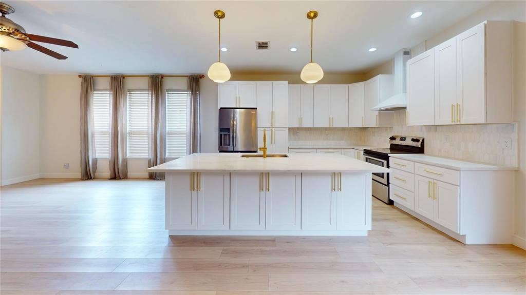 10514 Greenbriar Lane, Rowlett, TX 75089 Kitchen featuring white shaker-style cabinetry, quartz countertops, a central island with a built-in sink, gold-tone hardware, and wood-finish flooring
