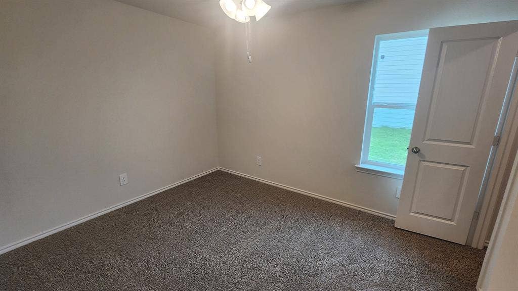 Neutral wall finishes, textured carpeting, a window, and a ceiling fan with integrated lighting
