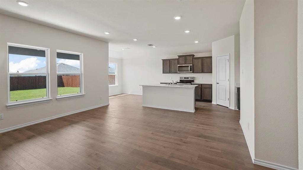 Open-concept interior featuring wood-finish flooring, recessed lighting, a central kitchen island, and dark-toned cabinetry