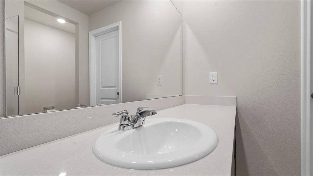 Bathroom vanity featuring a light-toned solid surface countertop, integrated oval sink, polished chrome centerset faucet, and an expansive frameless wall-mounted mirror