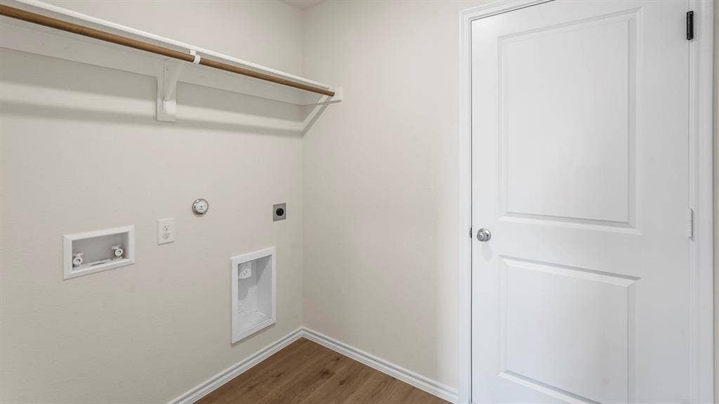 Utility area featuring wood-finish flooring, a white interior door, and a built-in wall shelf with a hanging rod