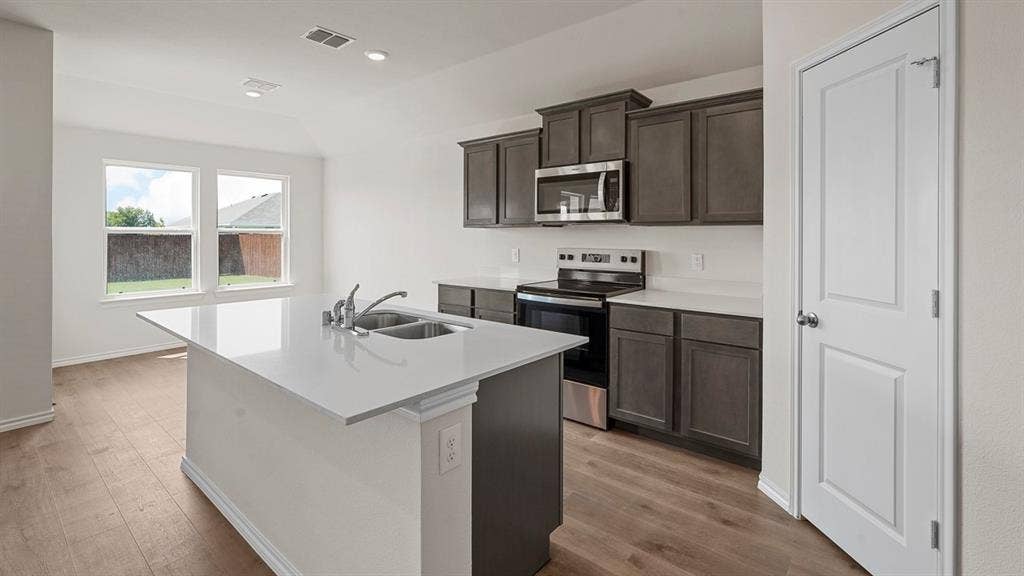 Kitchen featuring dark-toned cabinetry, a quartz-topped center island, stainless steel appliances, and wood-finish flooring