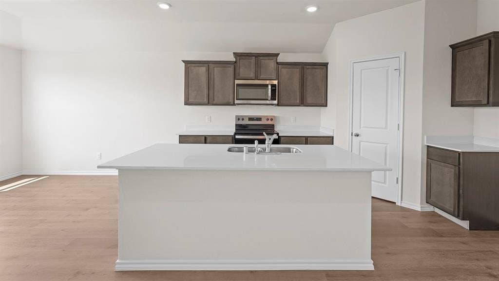 Kitchen featuring a large central island with a solid-surface countertop, dark-finish cabinetry, stainless steel appliances, and wood-finish flooring