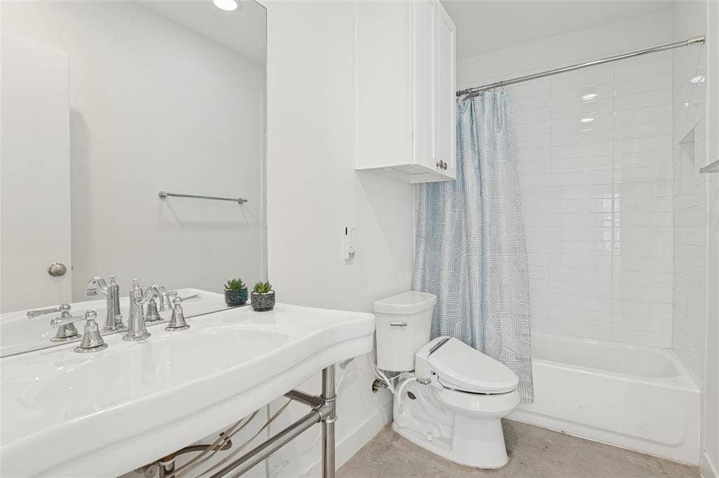614 Finley Court, Dallas, TX 75208 Bathroom featuring a wall-mounted vanity with a porcelain sink, polished metal faucet, white shaker-style wall cabinetry, and a shower-tub combination with subway tile surround