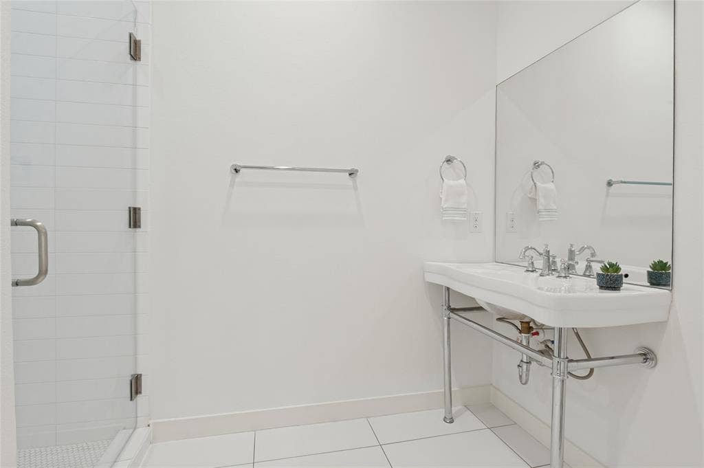 614 Finley Court, Dallas, TX 75208 Wall-mounted console sink with chrome finish legs and widespread faucet, glass-enclosed shower with horizontal wall tile, and large-format floor tile
