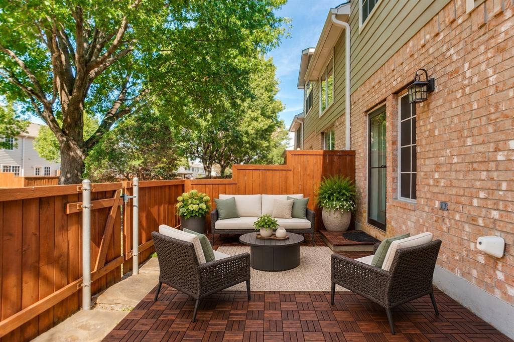 Rear exterior patio featuring wood-finish decking, privacy wood fencing, brick masonry, and attached wall-mounted lighting