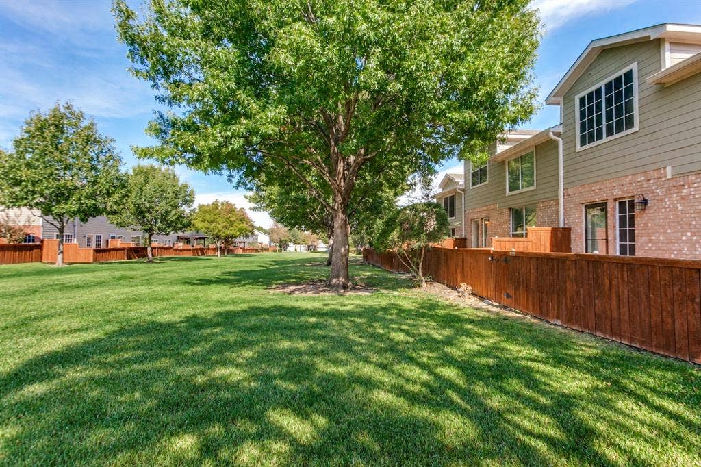 Expansive green space featuring mature trees and wood privacy fencing, complemented by a multi-story exterior with horizontal siding and brick masonry