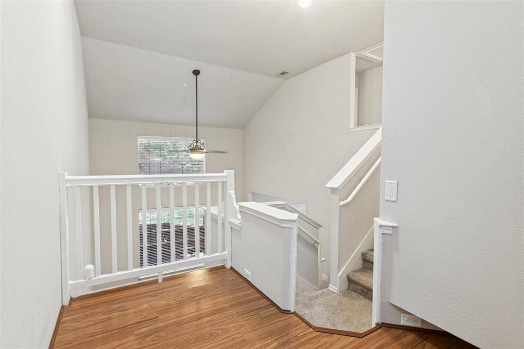 Vaulted ceiling featuring a central pendant light, wood-finish flooring, and white railings