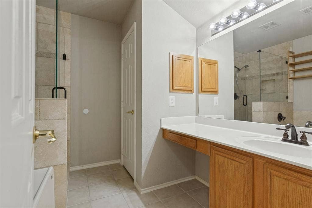 Bathroom featuring a vanity with a white countertop and oval under-mount sink, wood-finish cabinetry, a large wall-to-wall mirror, and a glass-enclosed shower with tiled walls