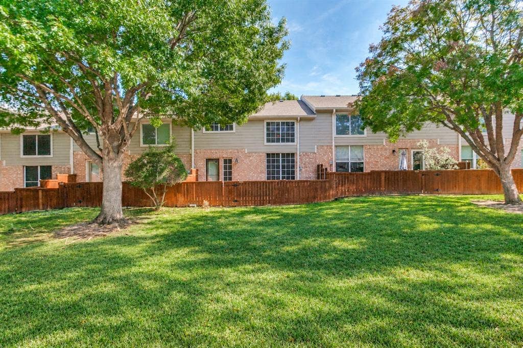 Exterior facade featuring mixed brick and siding, a wood privacy fence, and mature shade trees situated on a grassy lawn