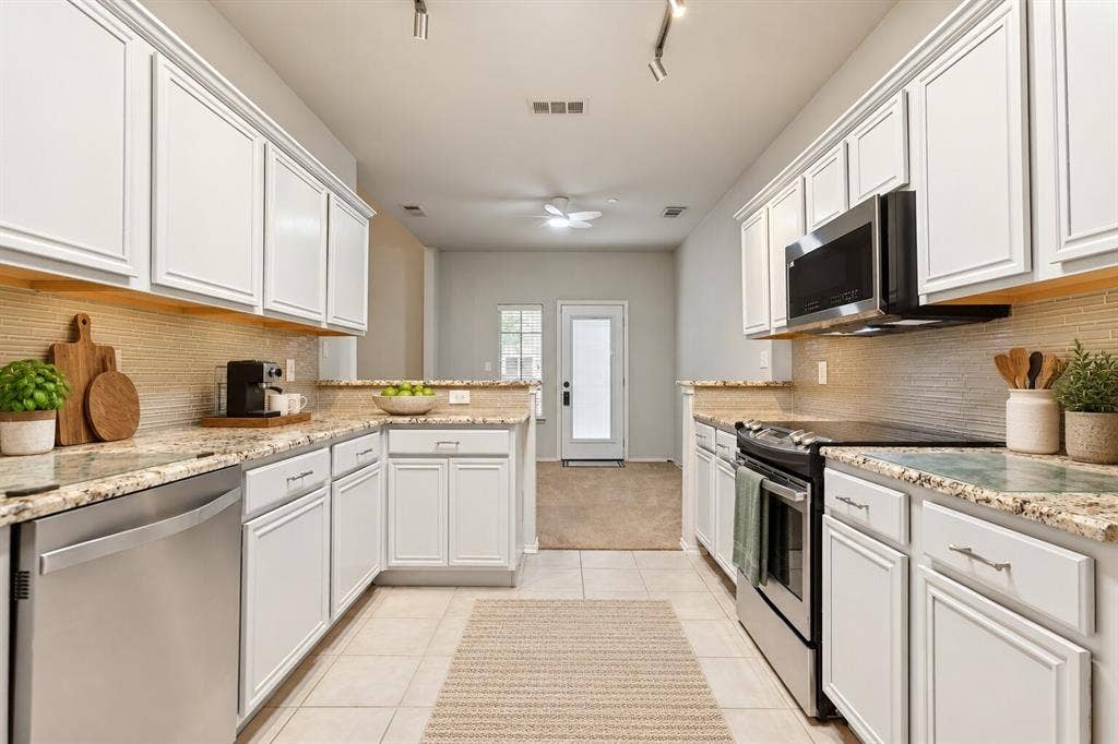 Kitchen featuring white shaker-style cabinetry, stone-finish countertops, textured tile backsplash, and stainless steel appliances