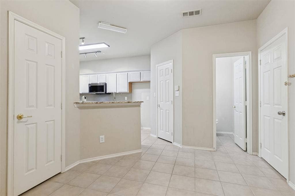 Interior area featuring neutral-toned tile flooring, multi-panel doors, and an open kitchen counter with stone-finish surfaces