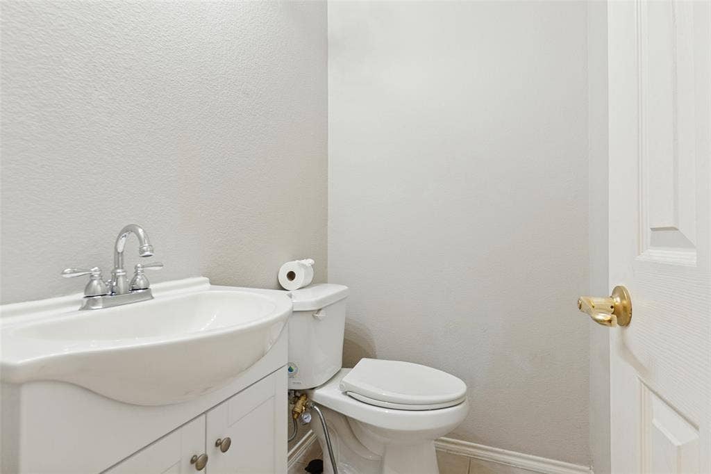 White vanity featuring a drop-in sink, chrome two-handle faucet, and built-in cabinet storage paired with a white toilet and a door with brass-tone hardware