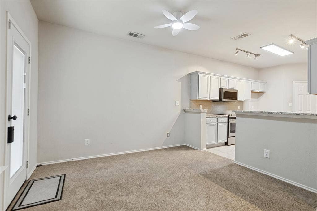 Open-concept kitchen area featuring white shaker-style cabinetry, stone-patterned countertops, a stainless steel built-in microwave, track lighting, and a multi-blade ceiling fan