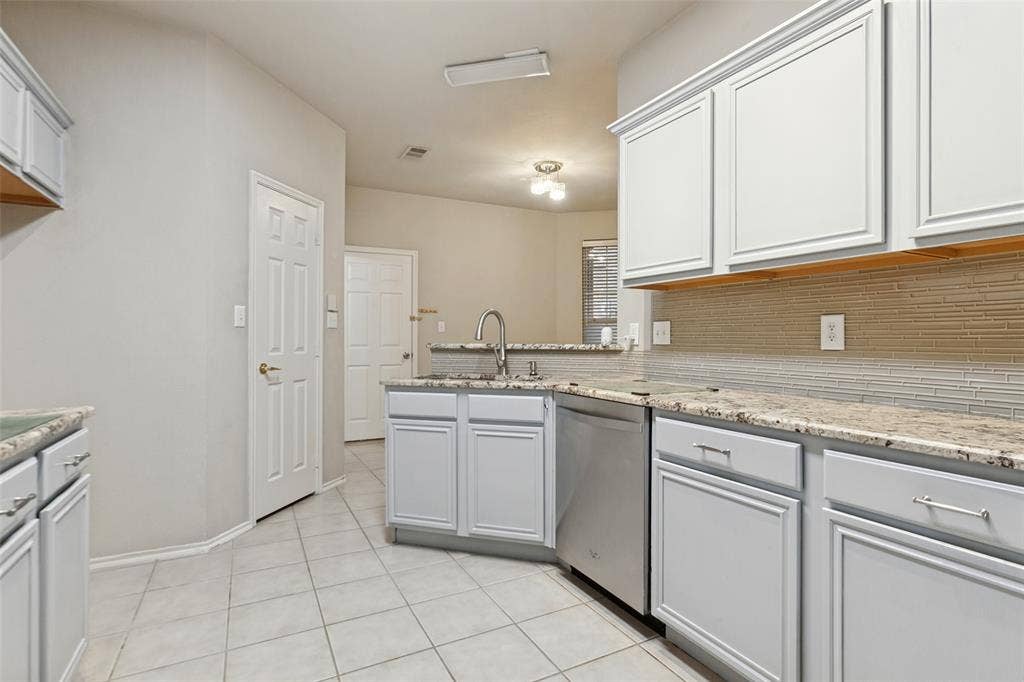 Kitchen featuring light-toned cabinetry, stone-finish countertops, tiled backsplash, stainless steel dishwasher, and ceramic tile flooring