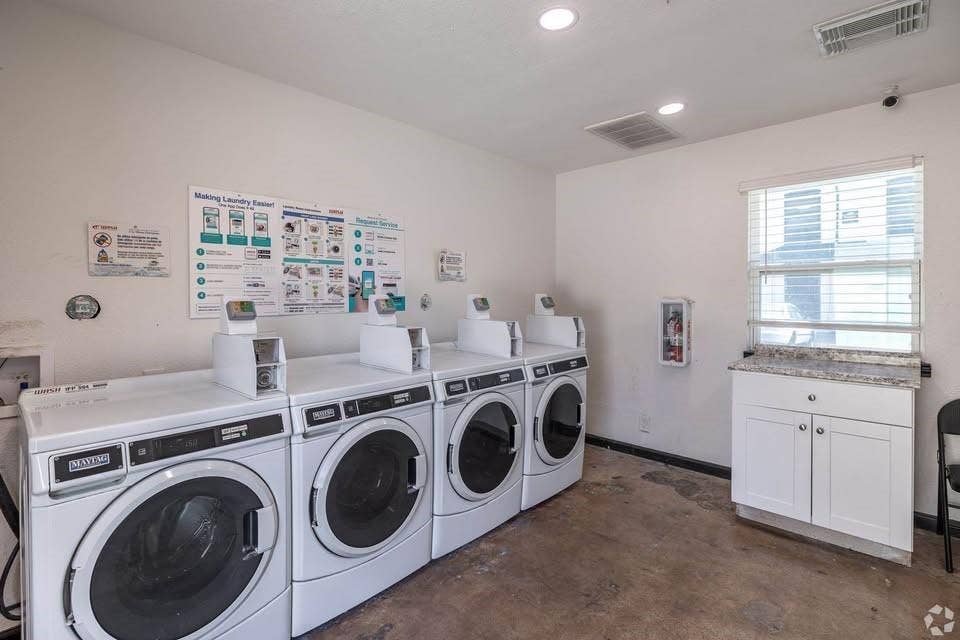 301 Rolston Road, #307-103, Irving, TX 75060 Shared laundry facility featuring four front-loading washers, a white cabinetry unit with a stone-finish countertop, and recessed ceiling lighting