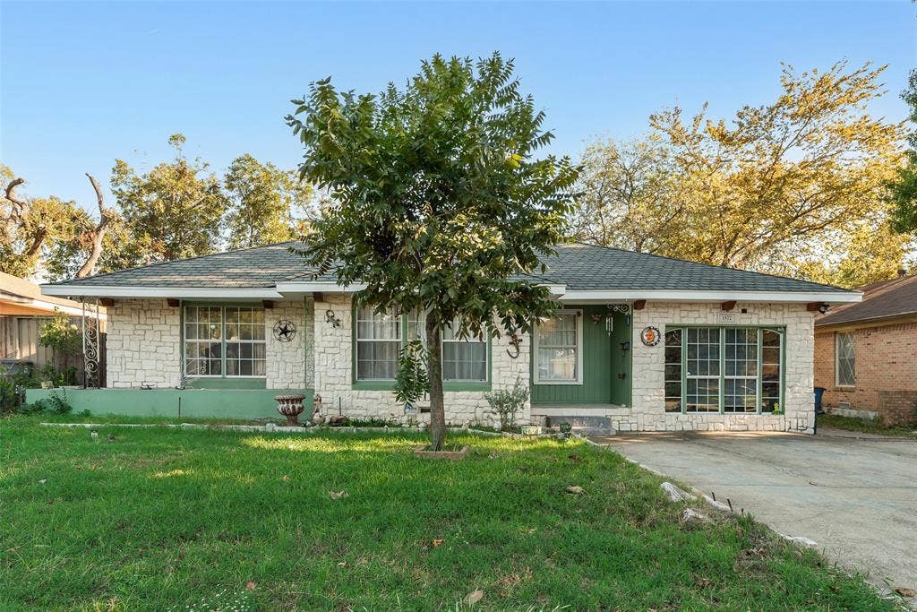 1572 Gillette Circle, Dallas, TX 75217 Single-story residence featuring a stone exterior, shingled hip roof, concrete driveway, multi-pane windows, and a covered entry