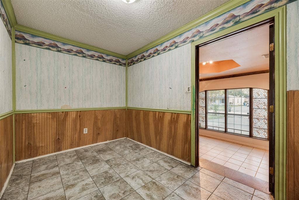 1572 Gillette Circle, Dallas, TX 75217 Interior space featuring stone-style tile flooring, wood-paneled wainscoting, and decorative wallpaper borders with painted wood trim