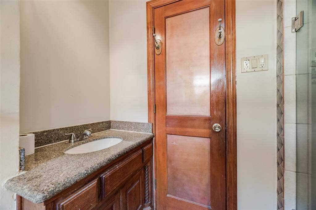 1572 Gillette Circle, Dallas, TX 75217 Vanity featuring a stone countertop with an integrated undermount sink, classic wood cabinetry, and an inset-panel solid wood door with brass-finish hardware