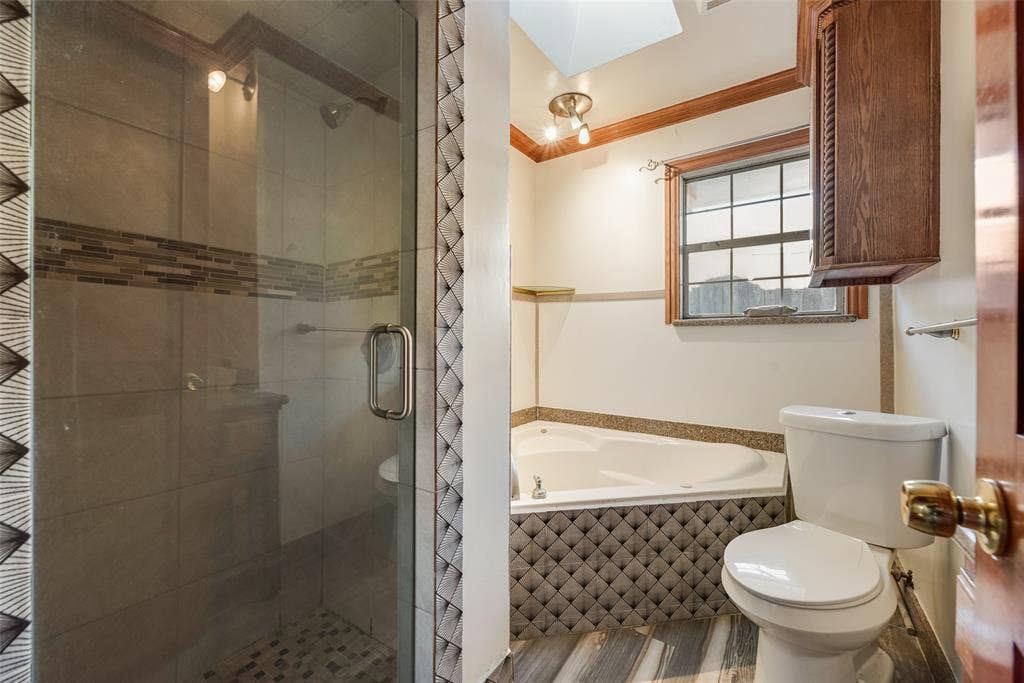 1572 Gillette Circle, Dallas, TX 75217 Bathroom featuring a glass-enclosed shower with a decorative tile inlay, a corner soaking tub with a patterned tile surround, and built-in wood-finish cabinetry