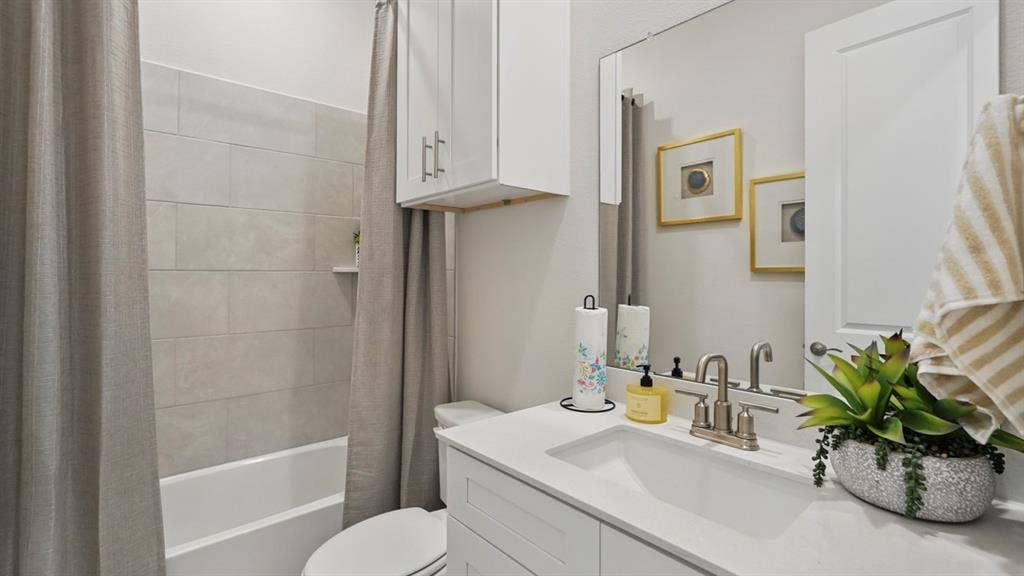 Bathroom featuring a single-basin vanity with a stone-composite countertop, subway-tile shower surround, wall-mounted storage cabinetry, and polished chrome hardware
