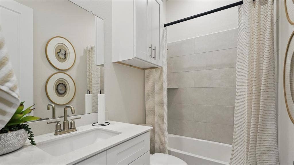 Bathroom featuring a white vanity with a solid-surface countertop, an integrated rectangular sink, brushed-nickel hardware, and a tub-shower combination with light-toned horizontal wall tile