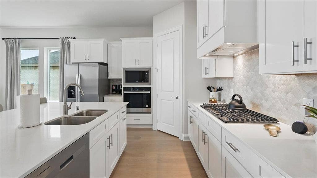 Kitchen featuring white cabinetry, quartz countertops, scalloped tile backsplash, wood-finish flooring, and stainless steel built-in appliances