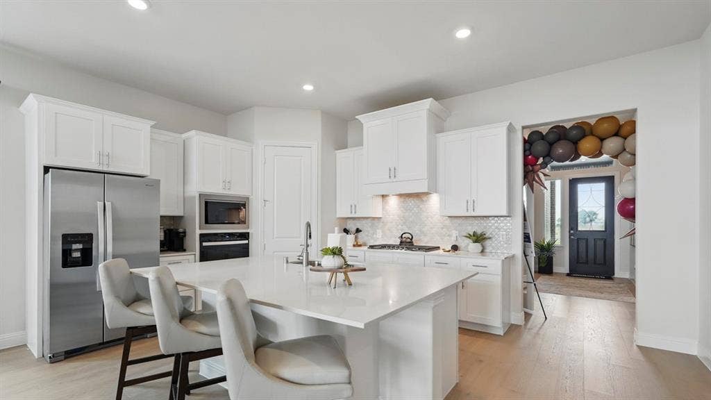 Kitchen featuring white cabinetry, solid-surface countertops, recessed lighting, built-in stainless steel appliances, and wood-finish flooring