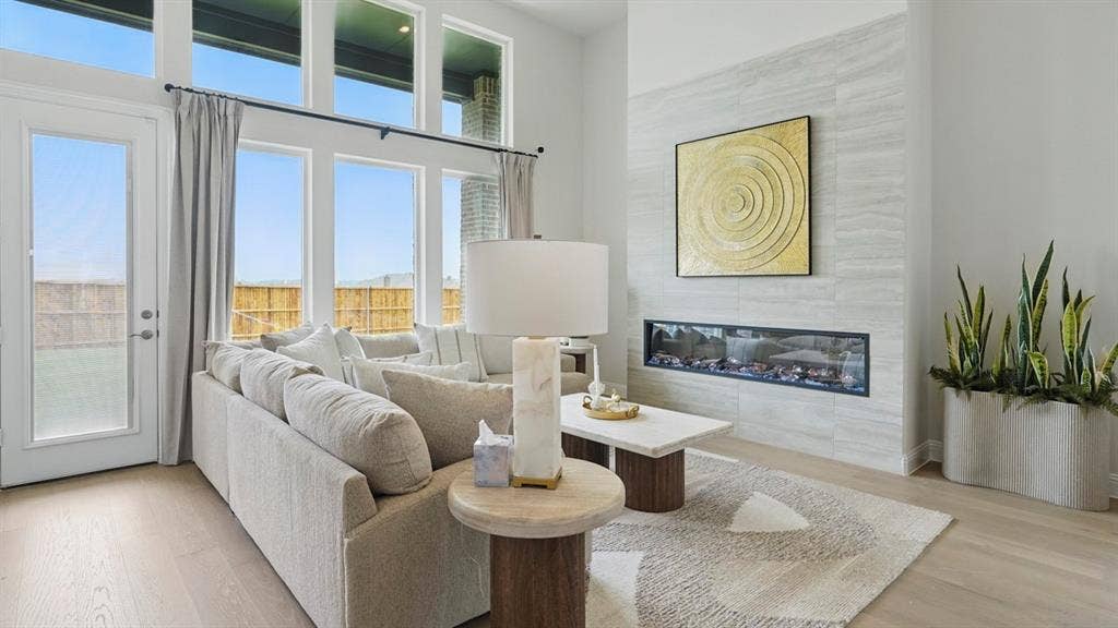 Living space featuring high ceilings, large multi-pane windows, wood-finish flooring, and a linear fireplace with floor-to-ceiling tile surround