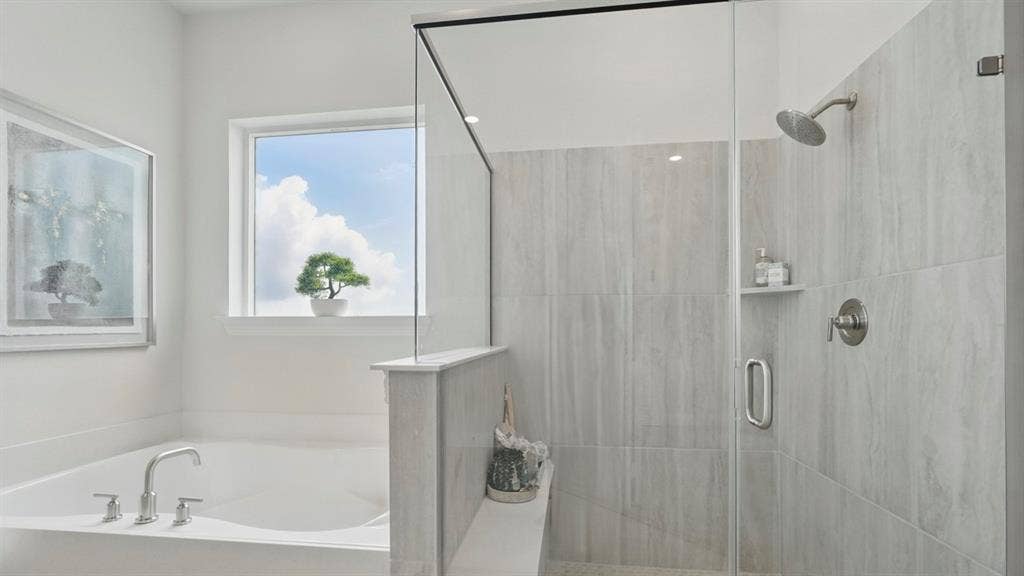 Soaking tub with chrome faucet, glass-enclosed shower featuring large-format tile surround, integrated shower shelving, and natural lighting from a window
