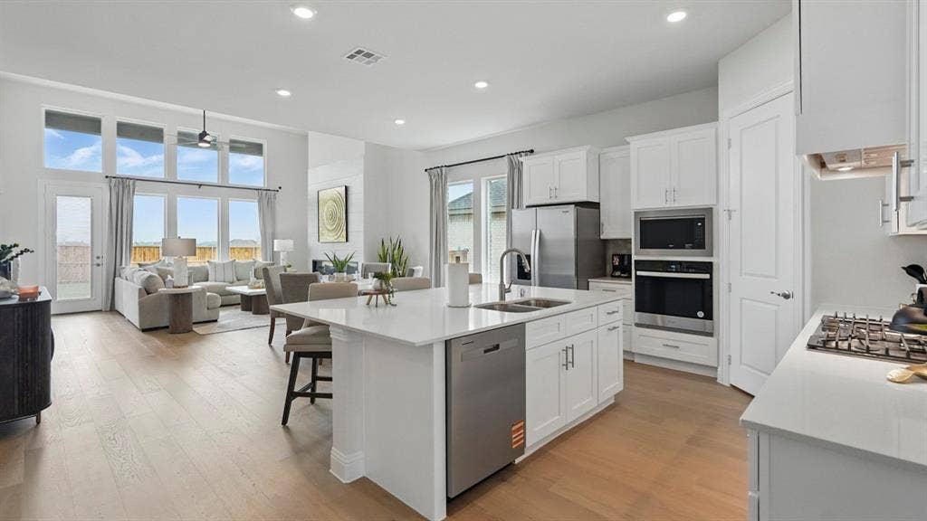 Open-concept kitchen featuring a central island with quartz countertops, stainless steel appliances, white cabinetry, and wood-finish flooring under high ceilings with recessed lighting