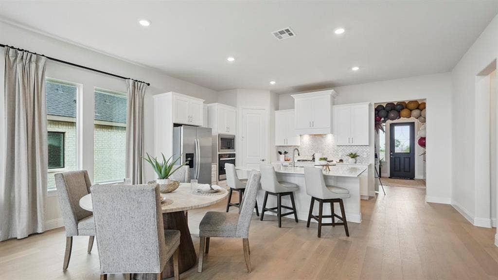 Open-concept kitchen featuring white cabinetry, a center island with stone-surface countertops, wood-finish flooring, and stainless steel appliances
