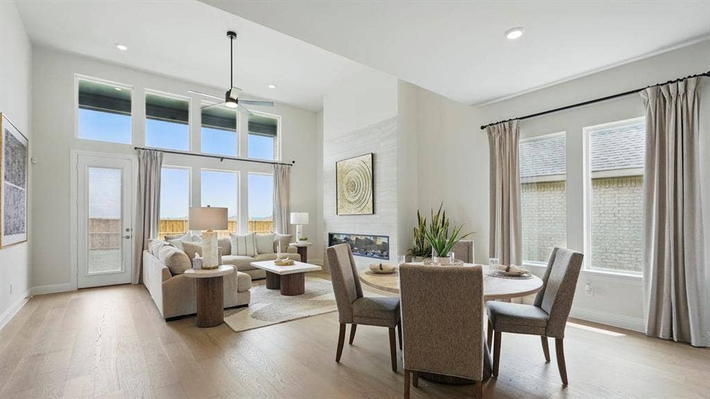 Open-concept living space with high ceilings, wood-finish flooring, floor-to-ceiling windows, and a built-in horizontal fireplace with stone surround