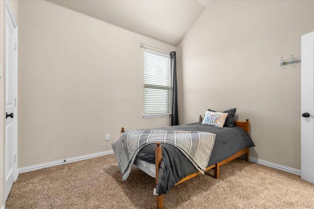 Vaulted ceiling, neutral wall tones, wall-to-wall carpeting, single-panel interior doors, and a window with horizontal blinds