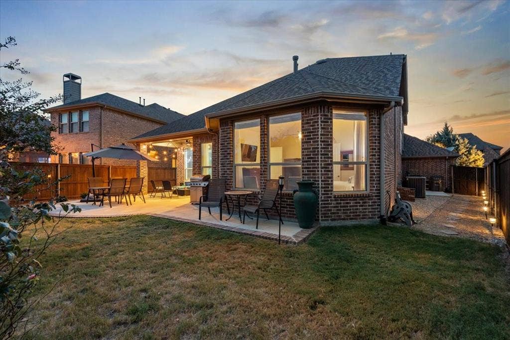 Brick exterior rear elevation featuring a covered patio, extensive hardscaping, and large-format windows