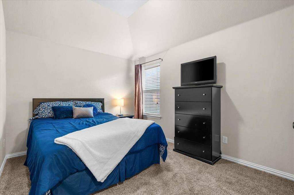 Vaulted ceiling, neutral wall tones, wall-to-wall carpeting, and a window with horizontal blinds