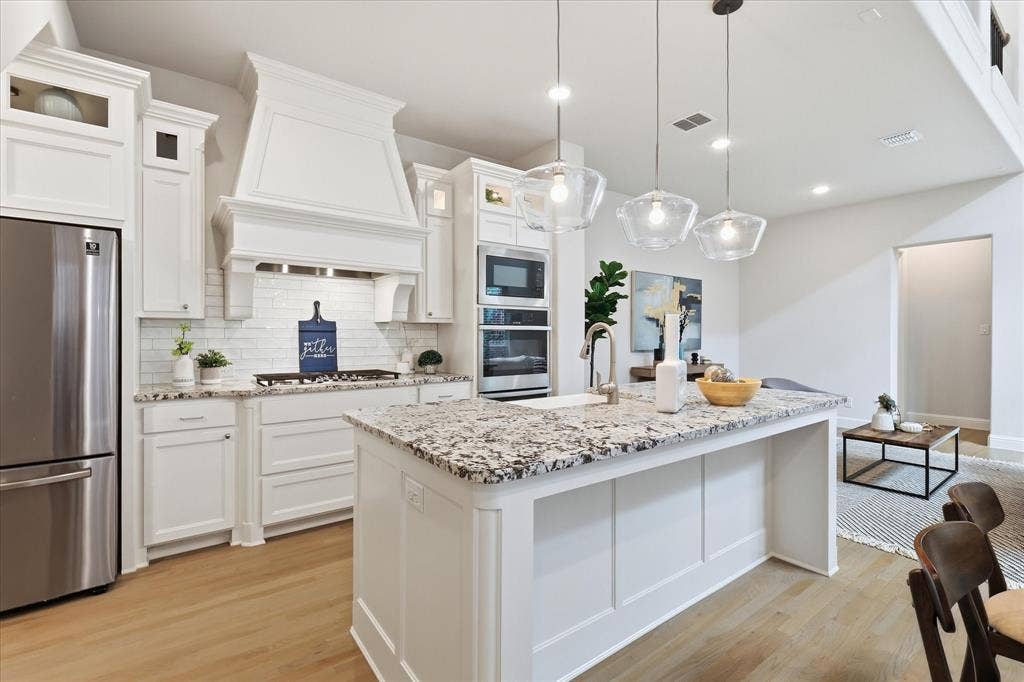 Kitchen featuring a central island with stone-finish countertops, white shaker-style cabinetry, custom range hood, stainless steel built-in appliances, and wood-finish flooring