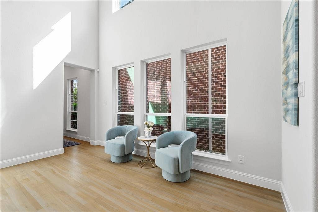 High-ceiling interior featuring wood-finish flooring, three vertical windows, and exposed exterior brick detailing