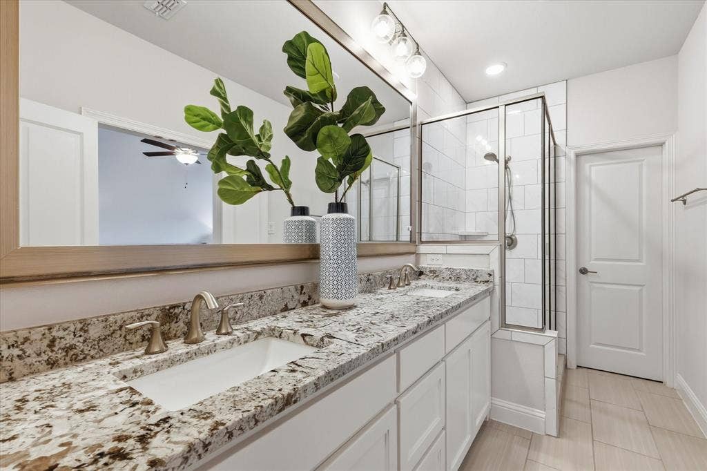 Dual-sink vanity with natural stone countertops, under-mount sinks, large-scale vanity mirror, and glass-enclosed shower with subway tile surround