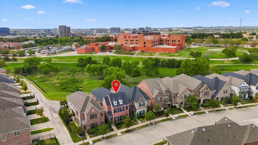 Aerial perspective showcasing a multi-story brick residence with a steep-pitched roofline and dormer windows, situated on a lot bordering expansive open green space
