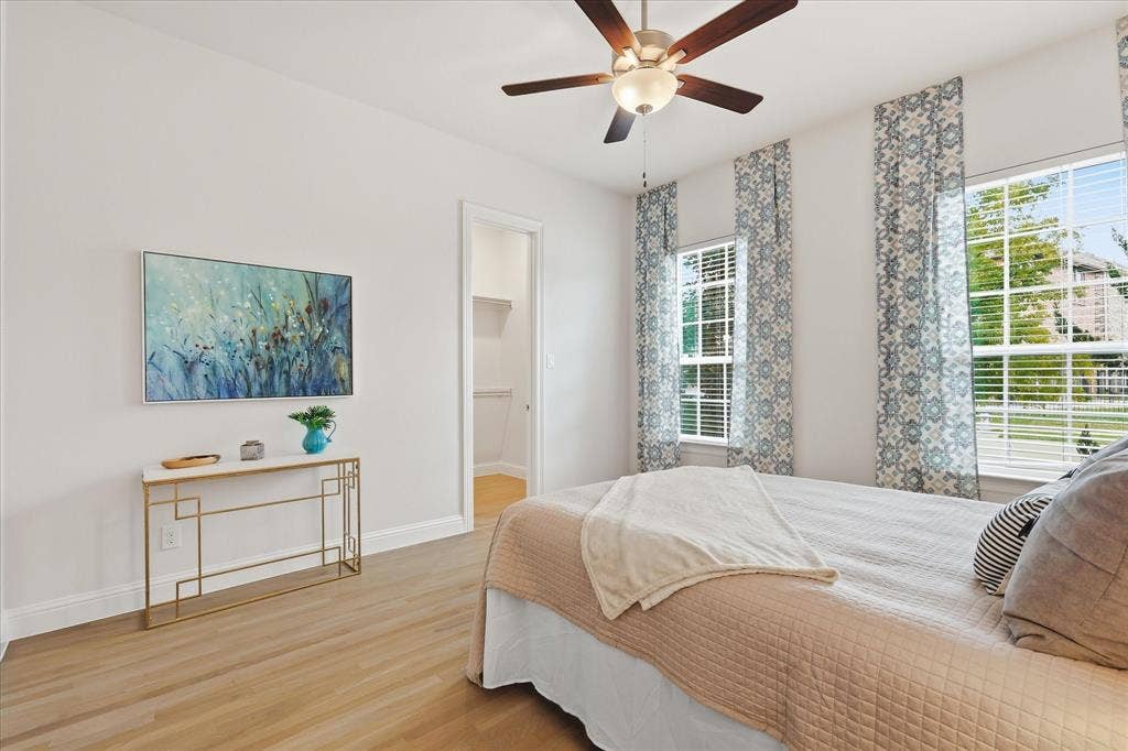 Bedroom featuring wood-finish flooring, a multi-blade ceiling fan with integrated lighting, dual windows, and an interior reach-in closet
