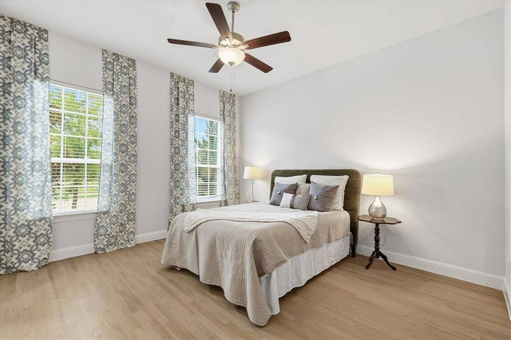 Light-filled room featuring wood-finish flooring, dual windows, and a central ceiling fan with an integrated light fixture