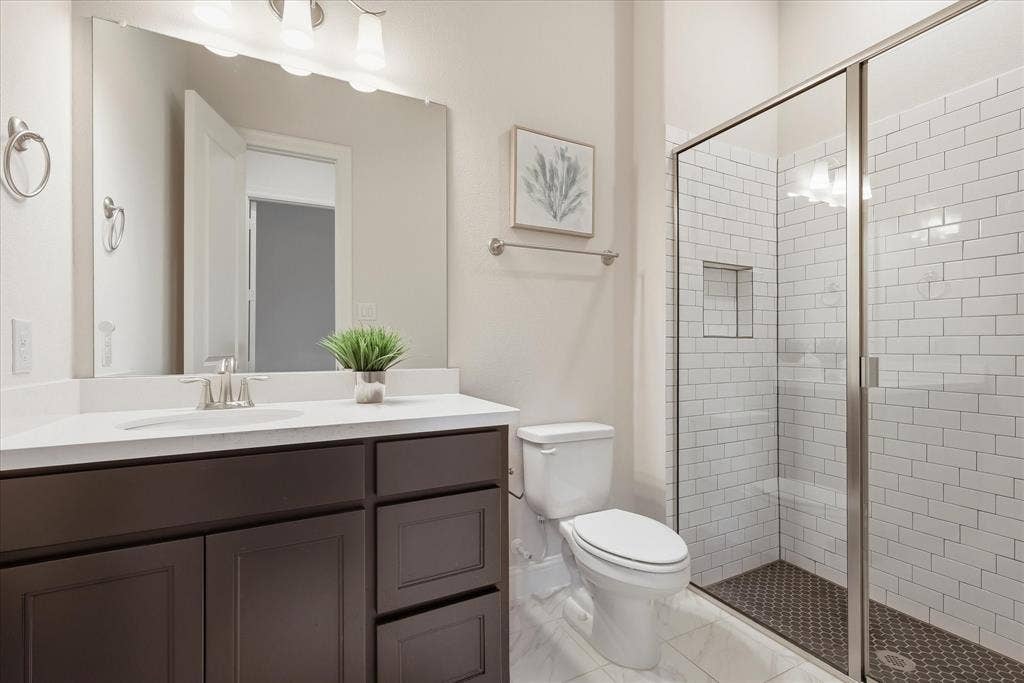 Dark cabinetry vanity with a light-toned countertop, framed wall mirror, and shower featuring white subway tile walls, a built-in recessed niche, and a glass enclosure