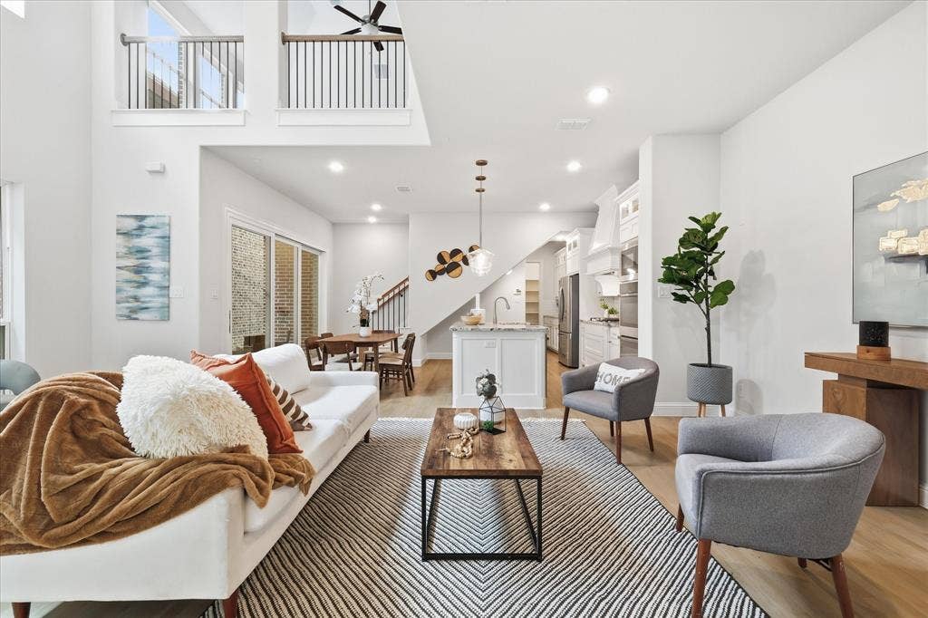 Open-concept interior featuring double-height ceilings, a central kitchen island with stone countertops, wood-finish flooring, recessed lighting, and a mezzanine-level balcony with metal railings