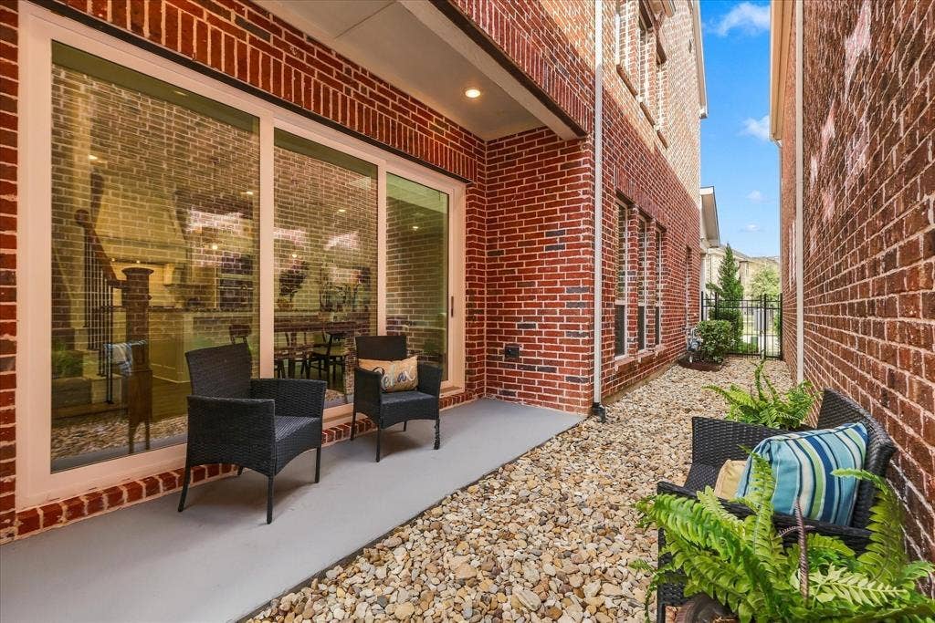 Exterior facade featuring red brick masonry, large sliding glass doors, a concrete patio, and a stone-covered ground surface