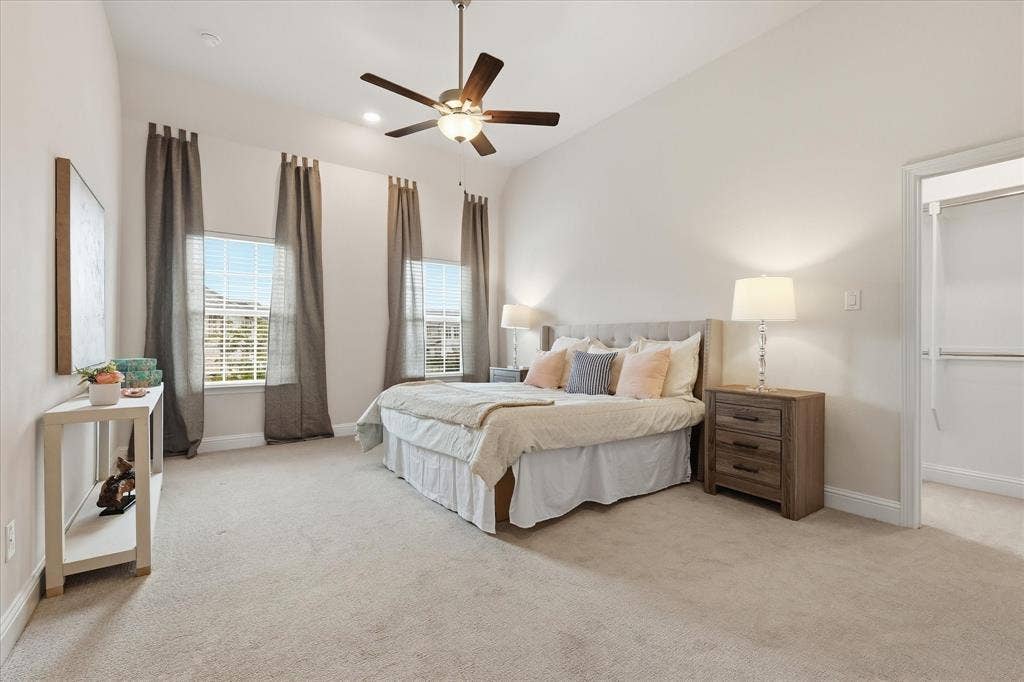 Room featuring high vaulted ceilings, neutral wall-to-wall carpeting, multiple windows, and a central ceiling fan