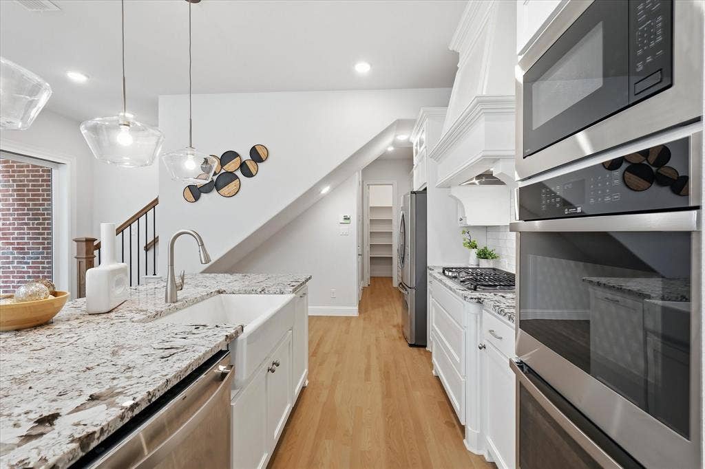 Kitchen featuring stone countertops, white cabinetry, a farmhouse-style sink, stainless steel wall-mounted oven and microwave, and wood-finish flooring